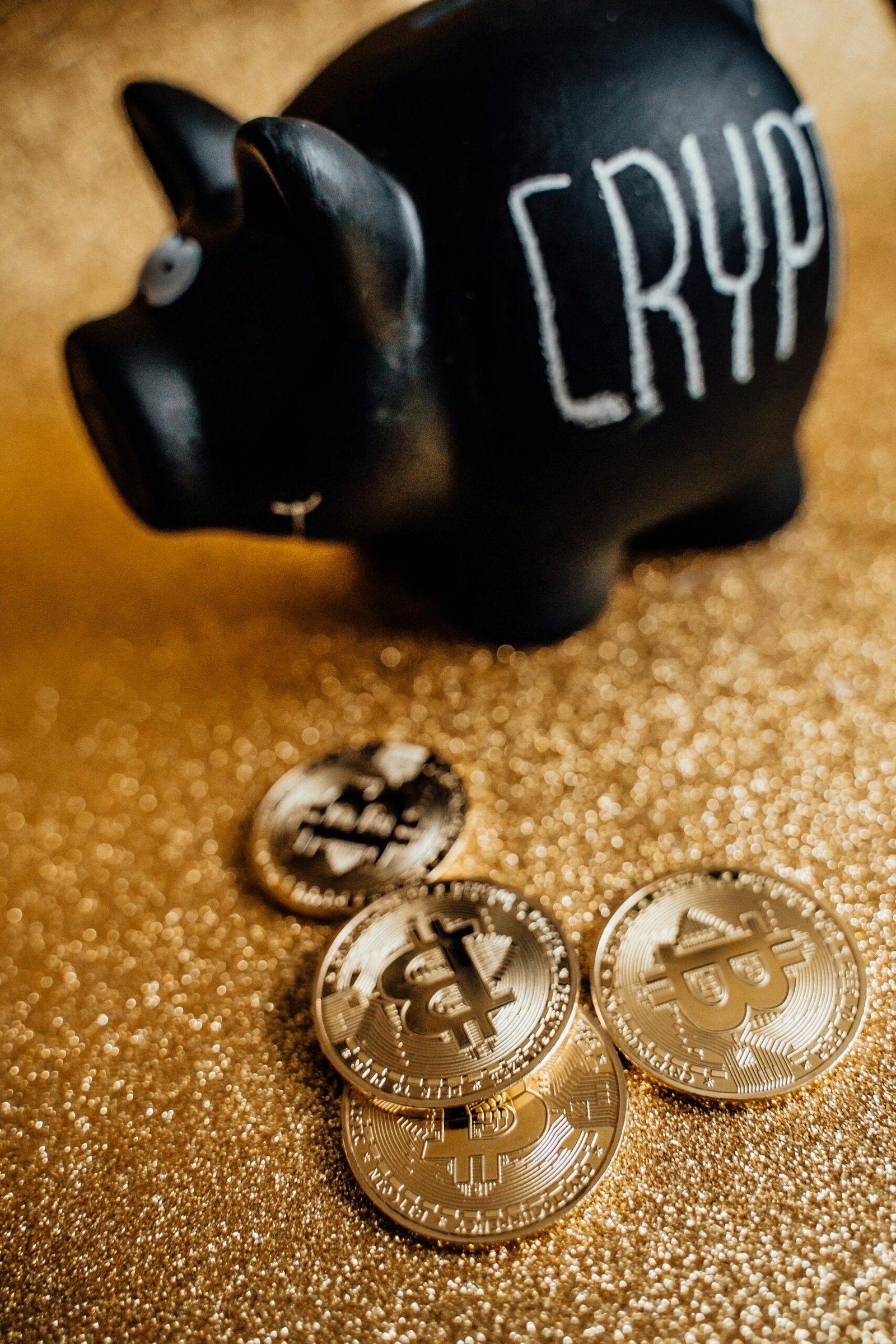 A black piggy bank labeled 'Crypto' with golden bitcoin coins on a sparkling gold surface.